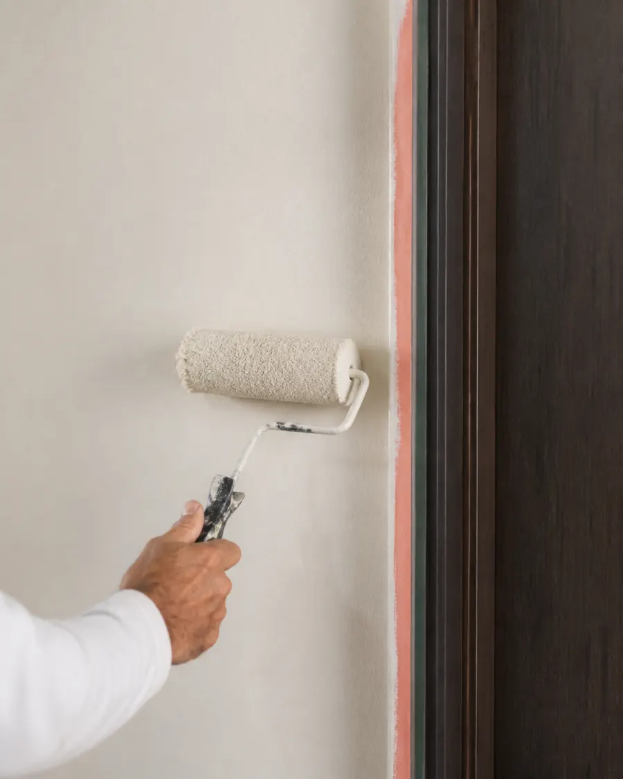 Painter rolling a smooth finish beside carefully masked dark wood trim